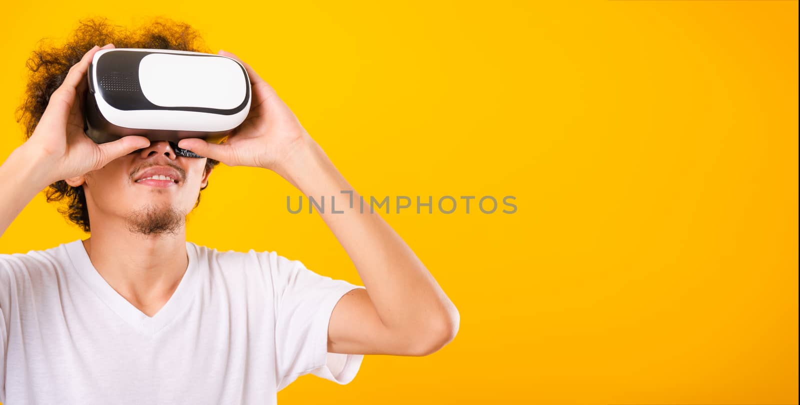 Asian handsome man with curly hair he using virtual reality headset or VR glass isolate on yellow background