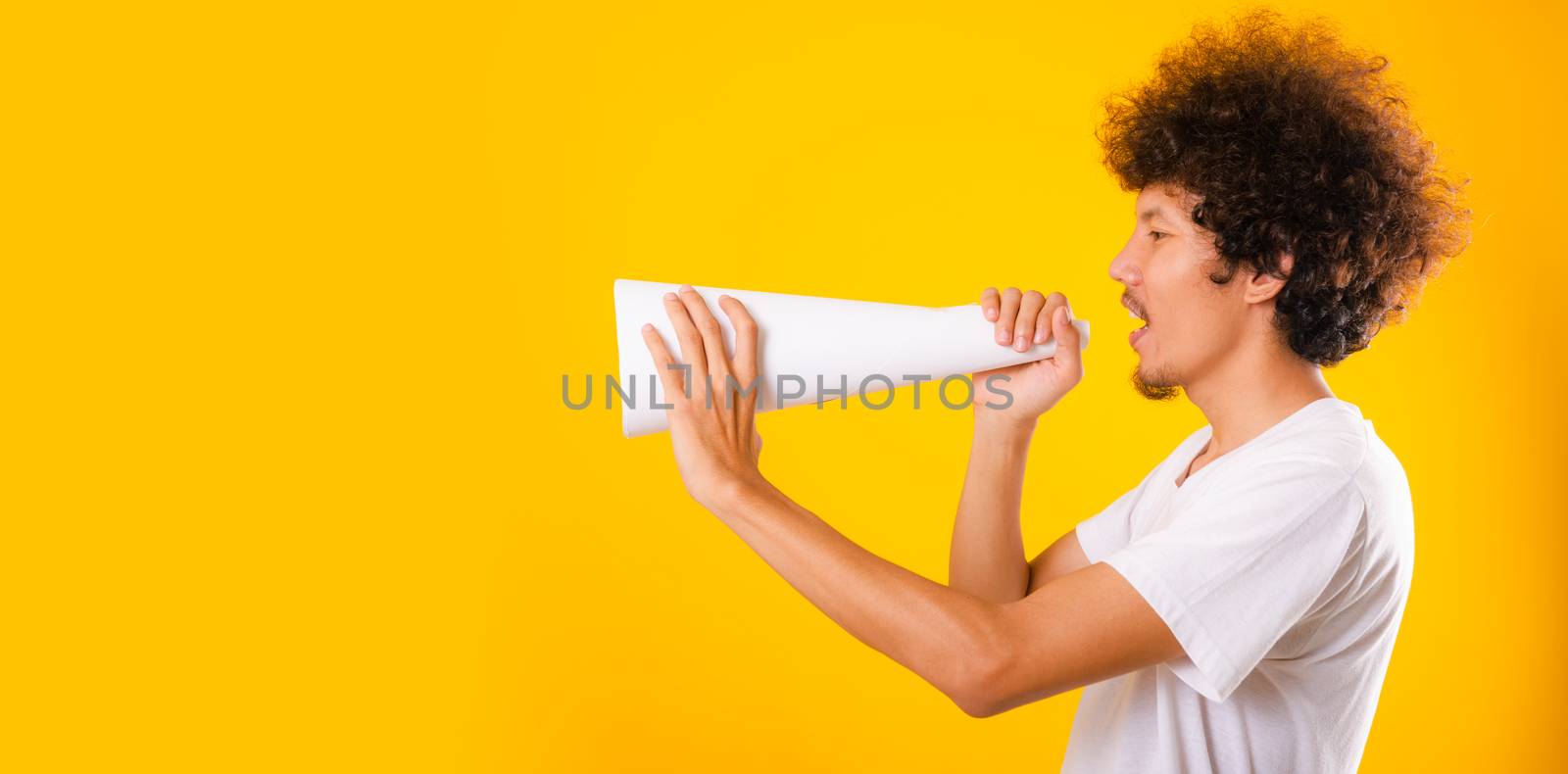 Asian handsome man with curly hair he announcing or spreading news using white speaker paper isolate on yellow background