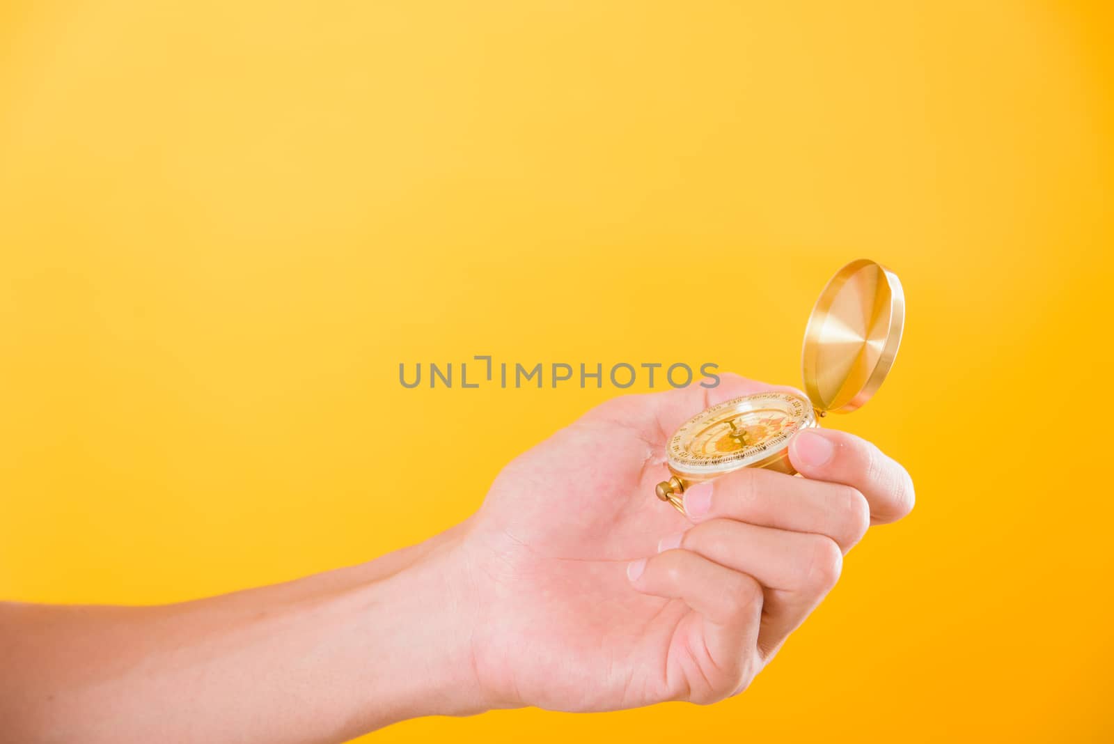 Hand holding antique brass compass isolated on yellow background with copy space for text