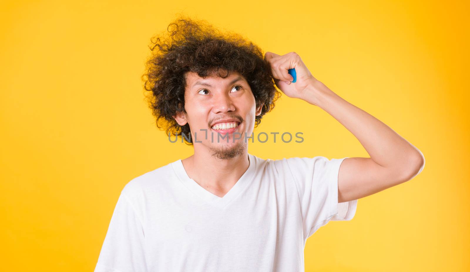 Asian man combing curly hair on yellow background by Sorapop