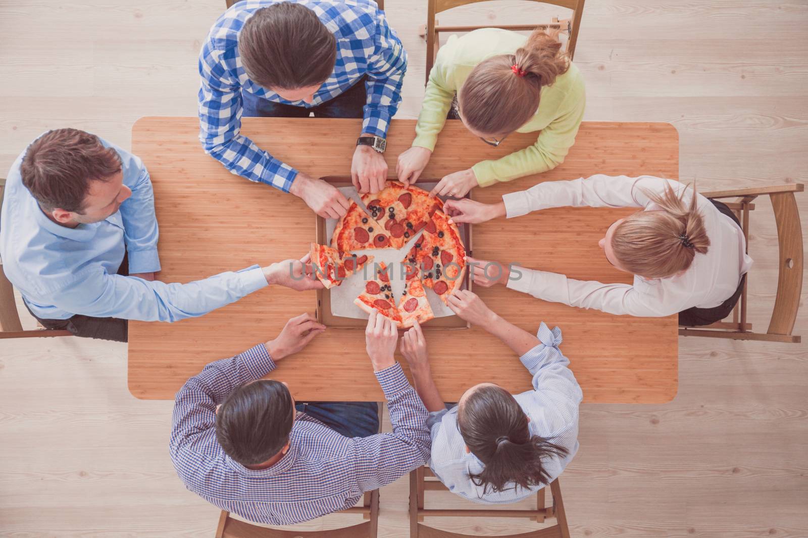 People taking pizza slices from wooden table, top view