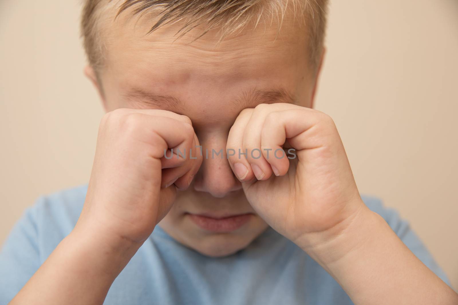 boy rubbing his eyes with his hands while he cries