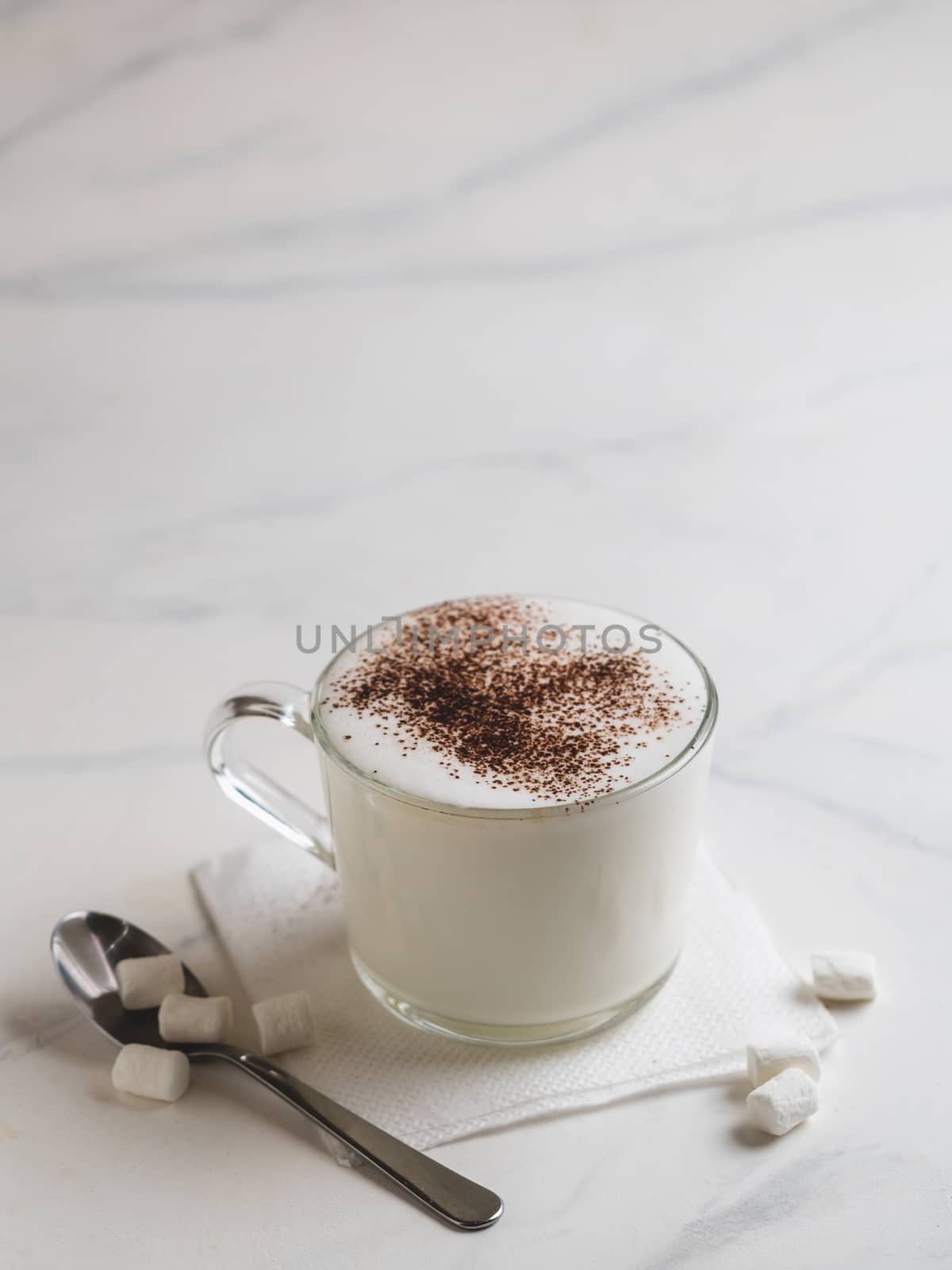 Babyccino - whipped milk or cream with cocoa or cinnamon powder and marshmallow. Idea and recipe for kids drink - warm whipped milk,without coffee. Babyccino in glass cup on marble table. Copy space