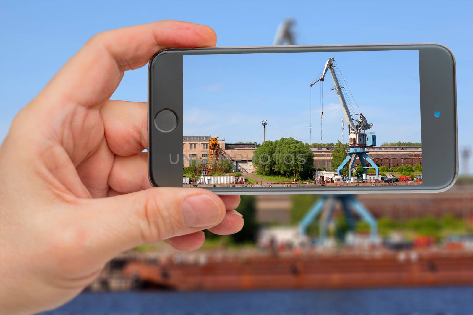 Cranes operate in river port. Construction crane in screen of smartphone. by sandipruel