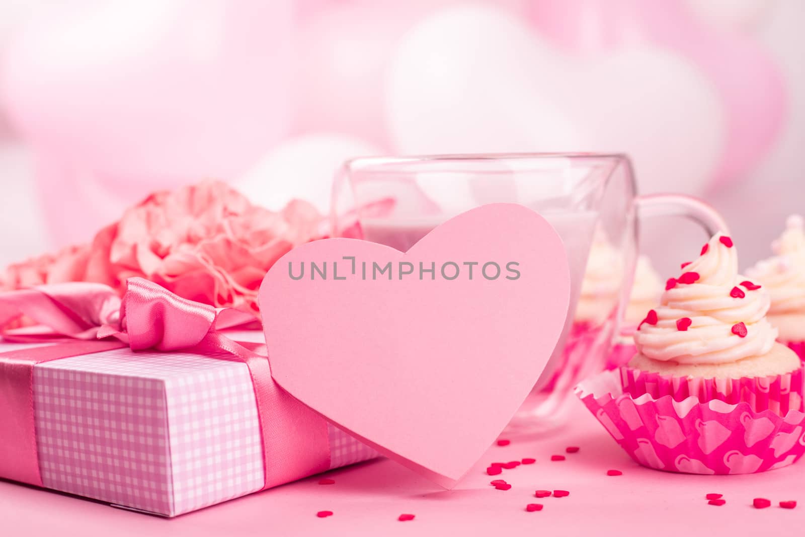 Valentine Day gift in a box wrapped in striped paper and tied with silk ribbon bow and heart shaped greeting card on pink balloons background with copy space for text