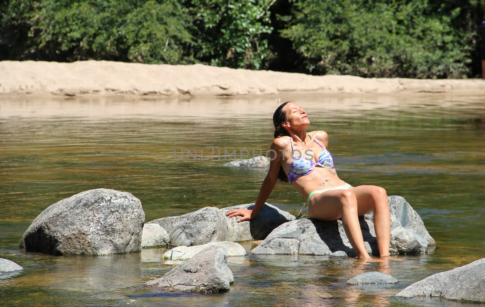 beautiful young woman sunbathing on the rocks of the mountain river