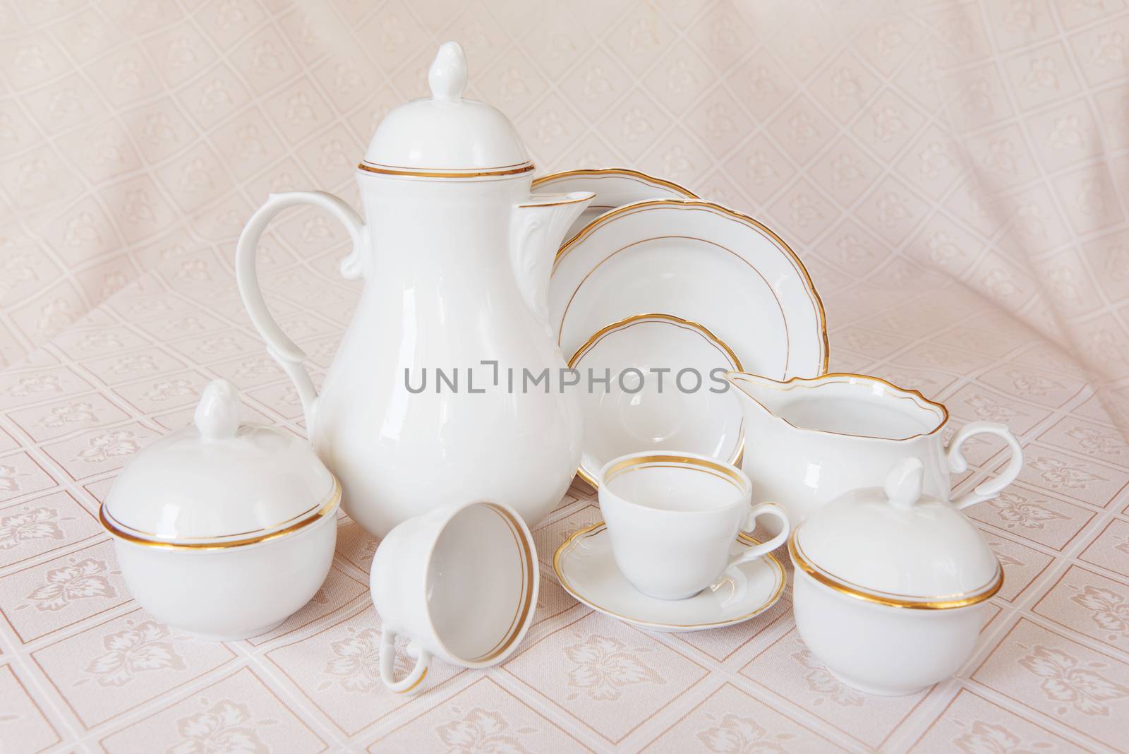 Classic white crockery for tea ore coffee: teapot, coffee pot, cup, serving plate, sugar bowl and creamer on a beautiful tablecloths
