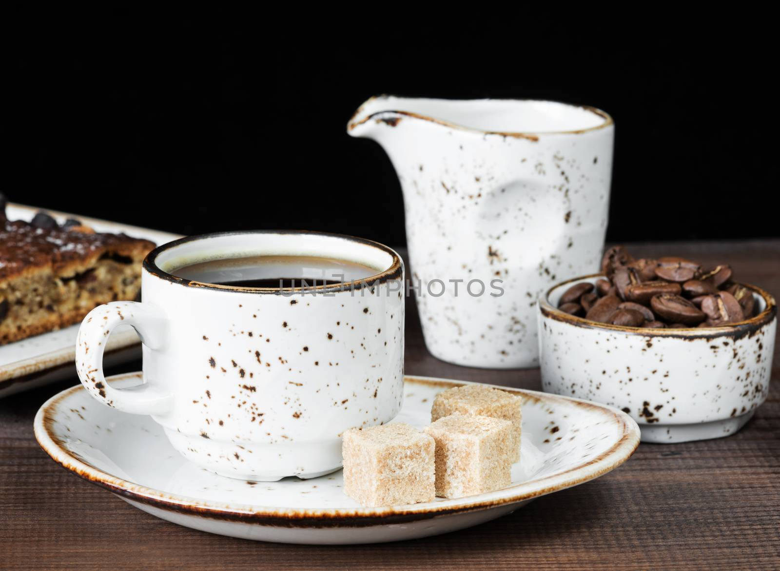 Vintage ceramic cup of coffee, coffee beans, cane sugar and a piece of chocolate cake