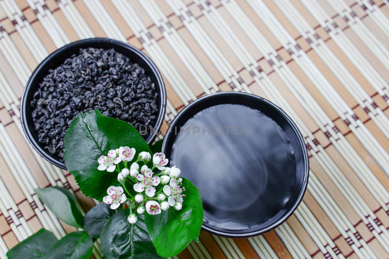 Two ceramic cups with green tea on a straw mat and white flowers, top view