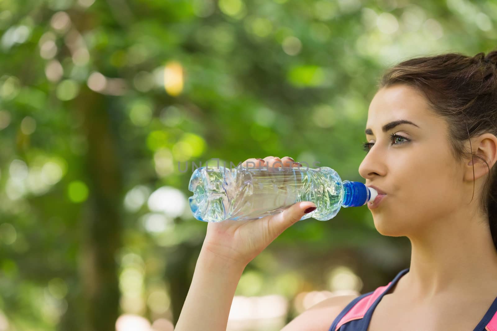 Sporty woman drinking water outdoors in a forest on a sunny day