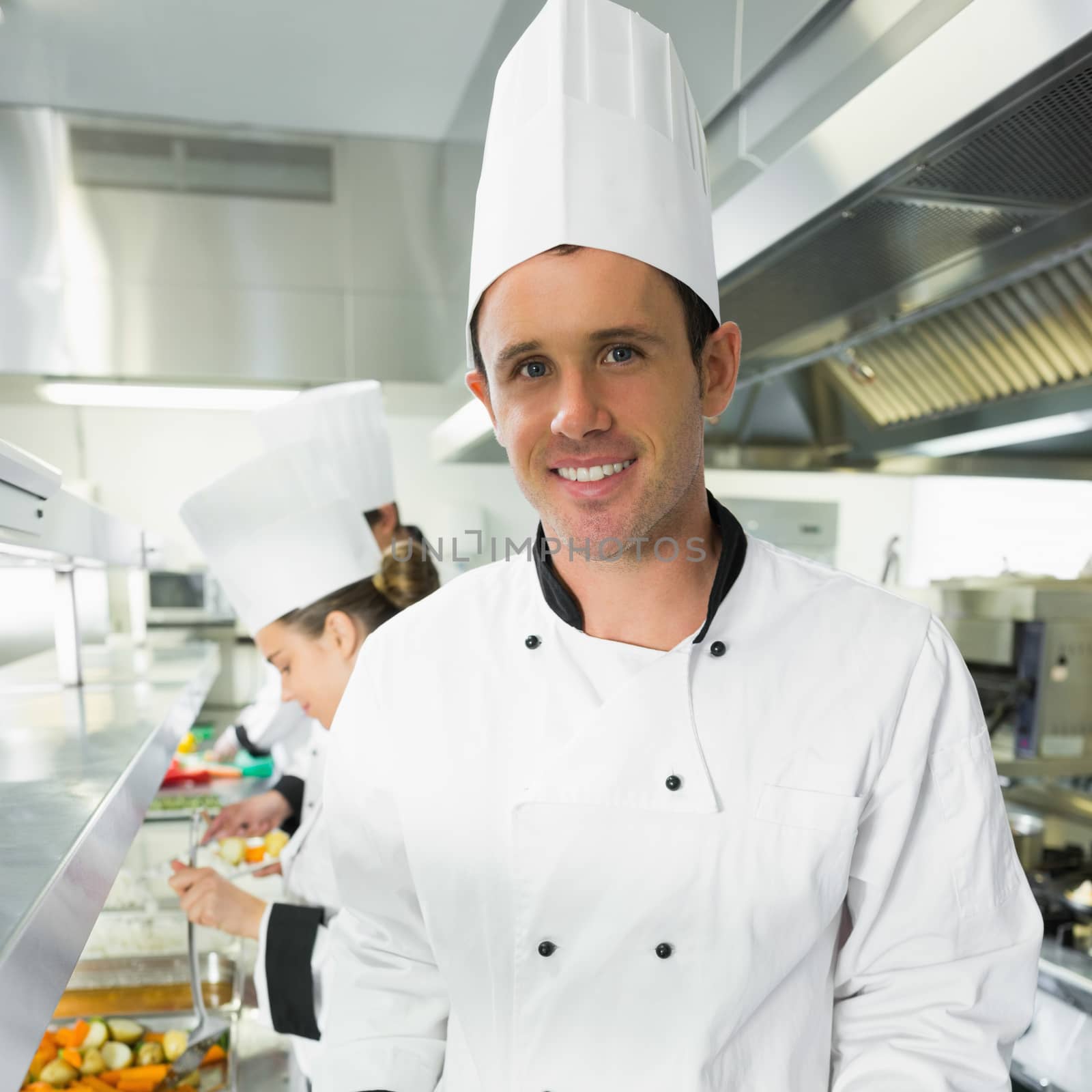 Handsome male chef posing in the kitchen smiling at the camera