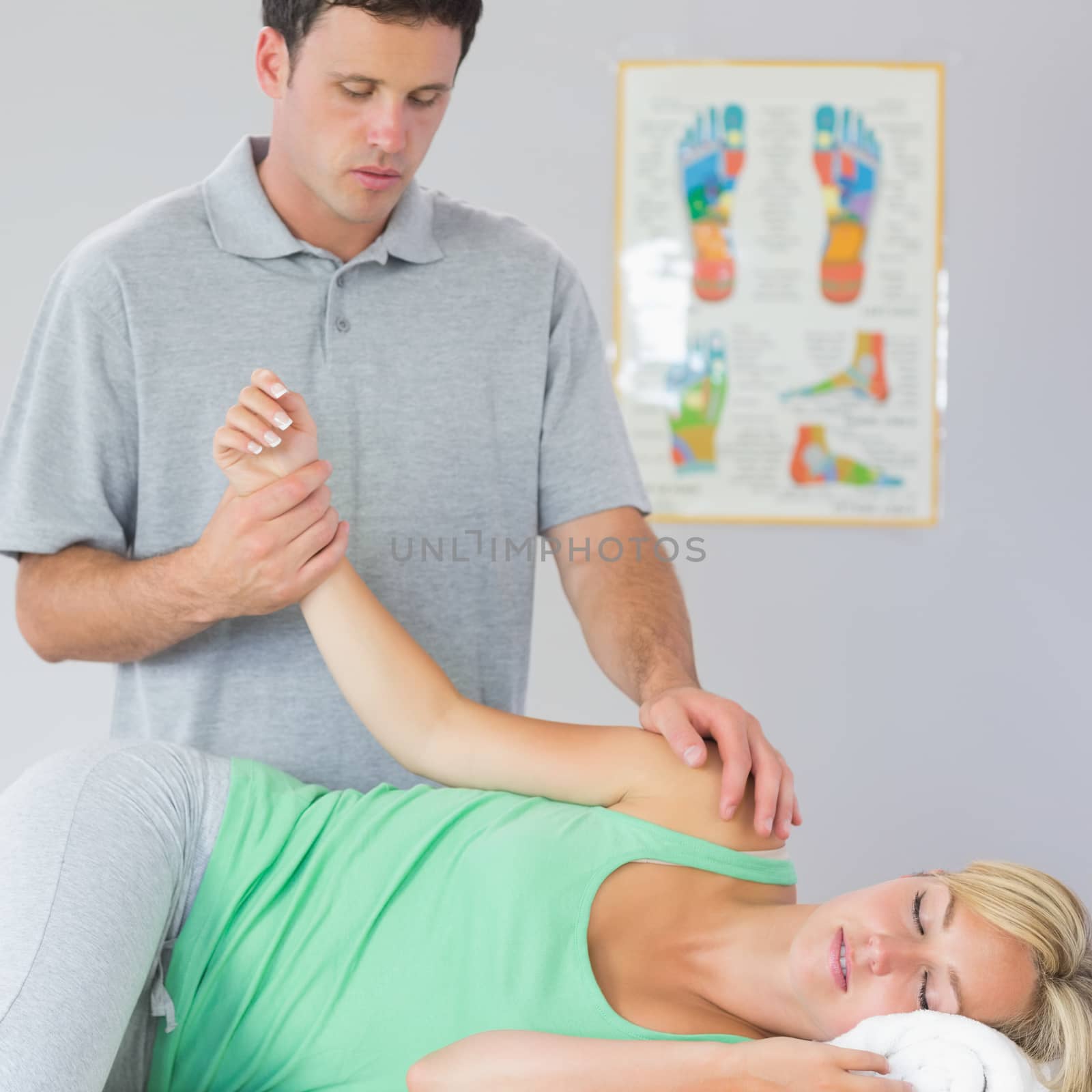 Handsome physiotherapist treating patients arm in bright office