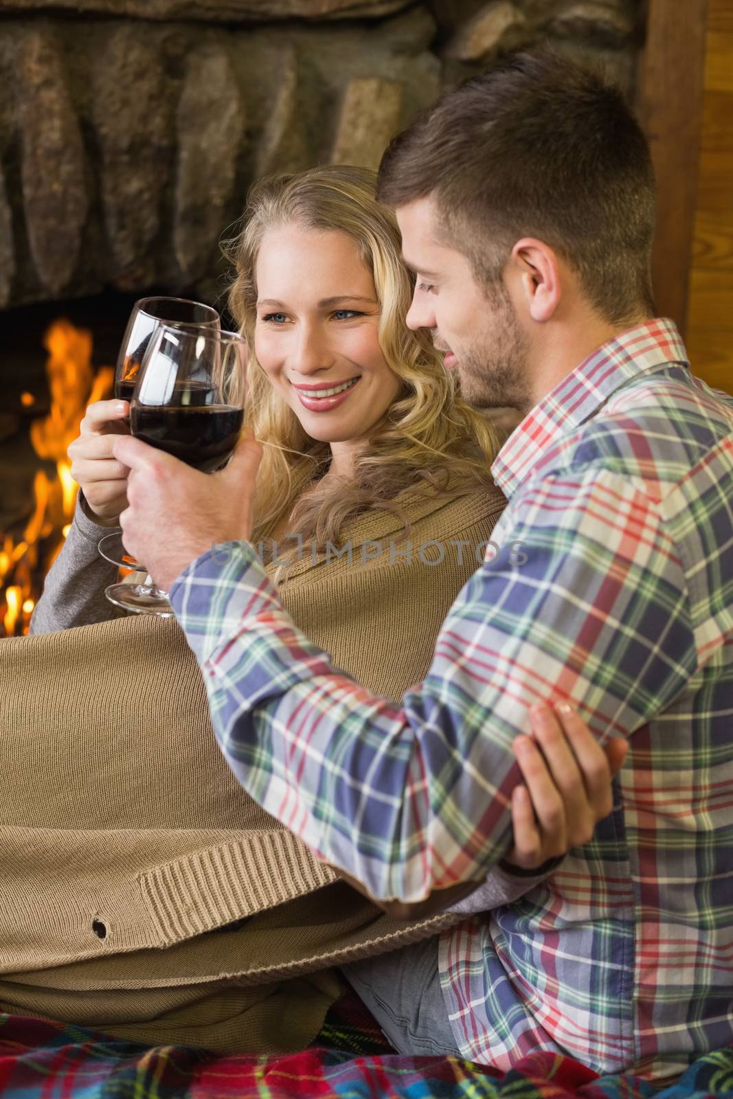 Couple toasting wineglasses in front of lit fireplace by Wavebreakmedia