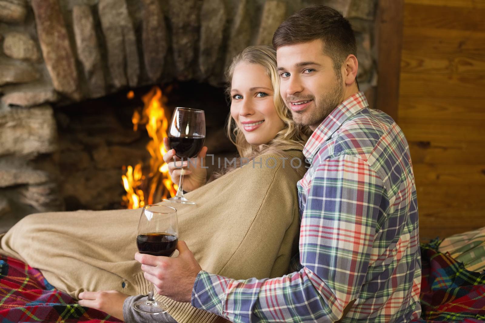 Rear view portrait of a romantic young couple with wineglasses in front of lit fireplace