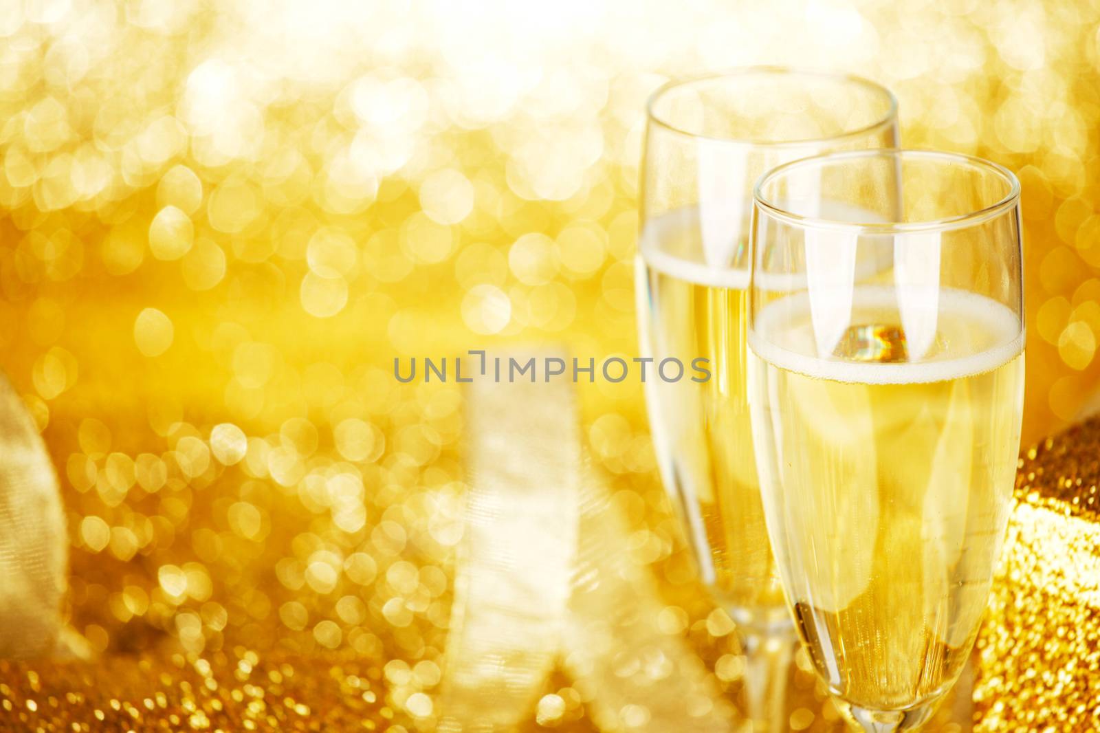 Champagne in glasses and gift box on golden background with twinkle lights