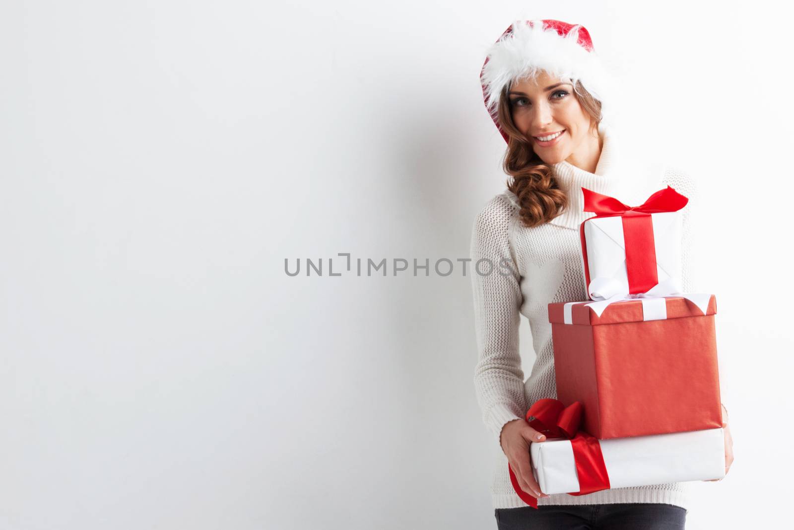 Happy woman in Santa hat with stack of Christmas gifts