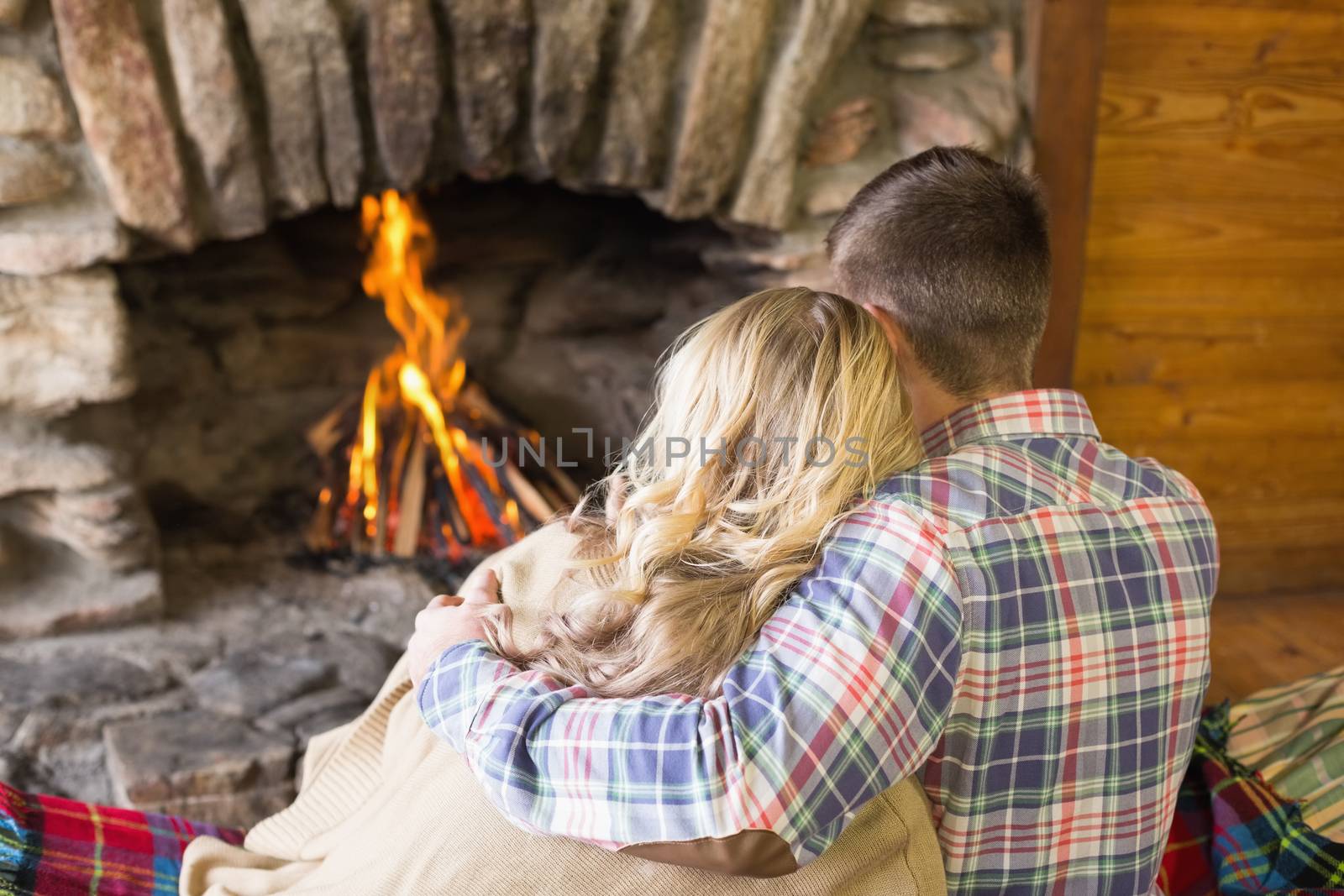 Rear view of a romantic young couple sitting in front of lit fireplace