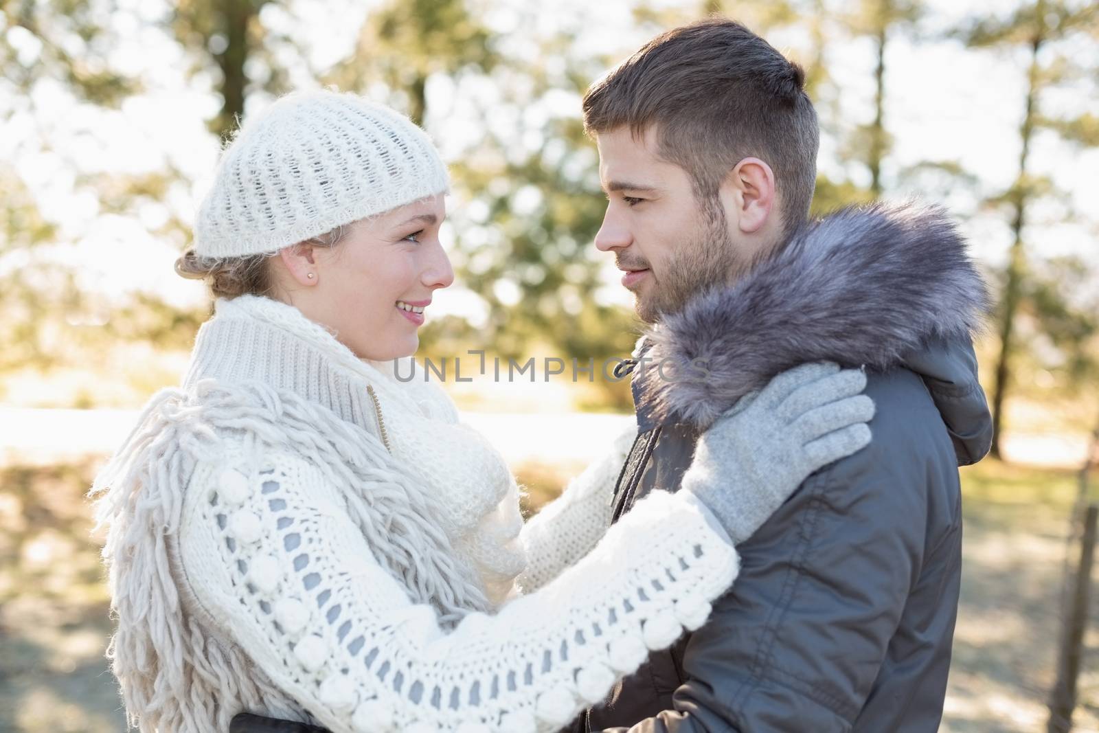 Side view of a loving young couple looking at each other in winter clothing in the woods