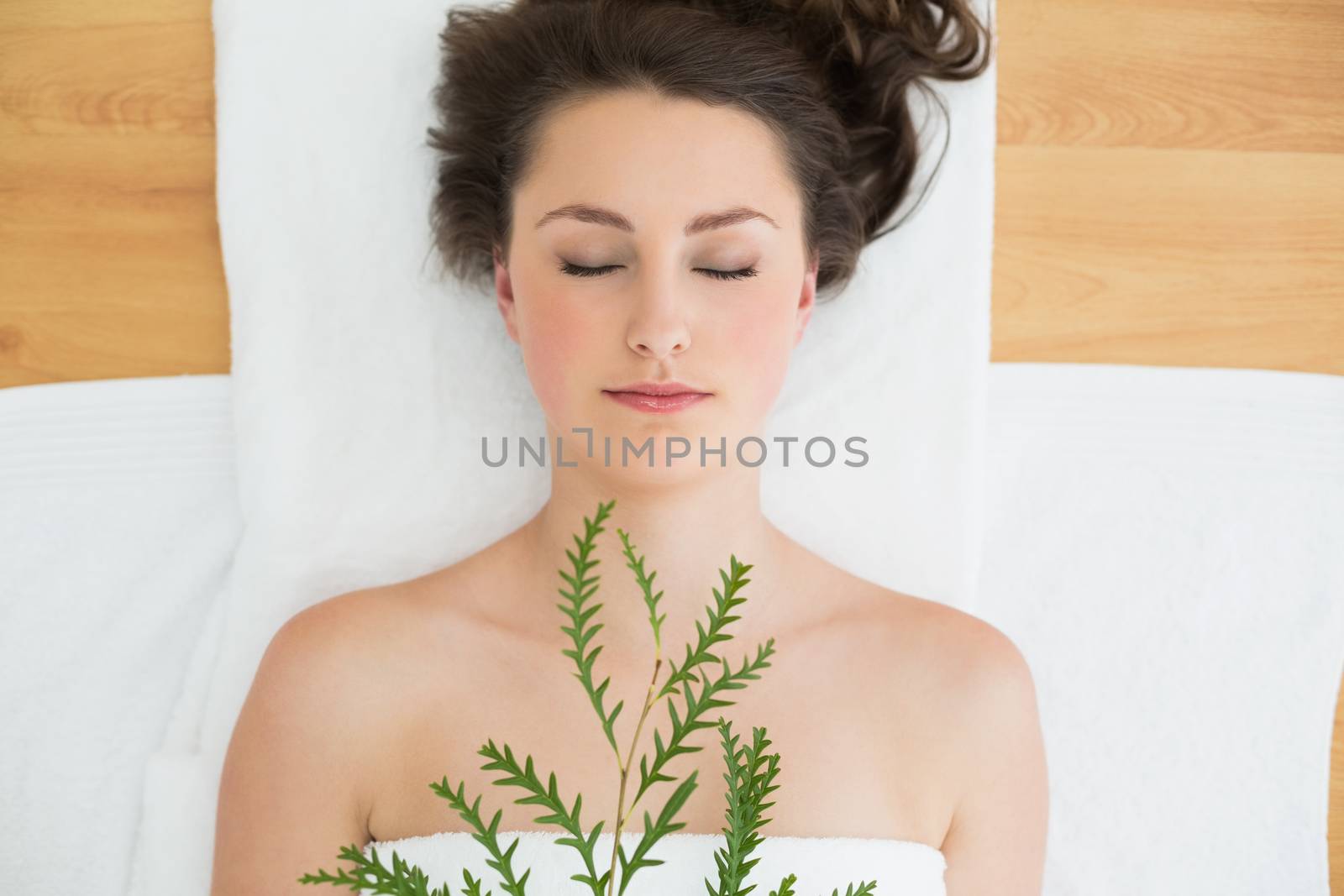 Overhead view of a young brunette lying with leaves on massage table in beauty salon