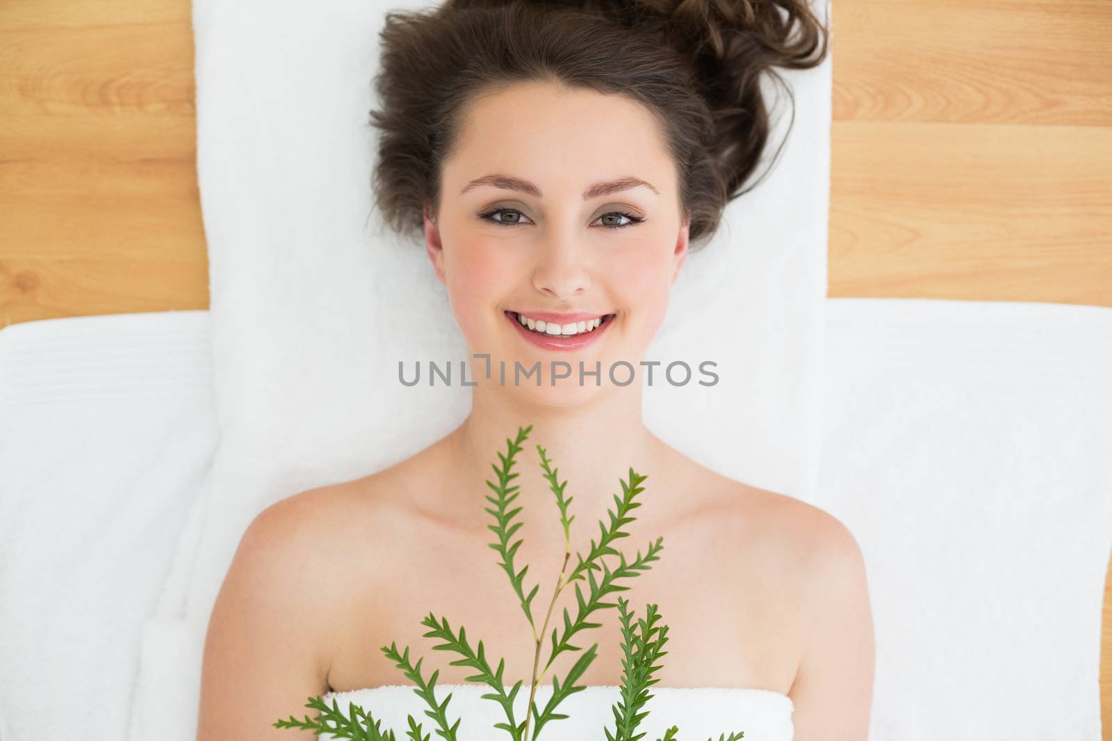 Overhead portrait of a young brunette lying with leaves on massage table in beauty salon