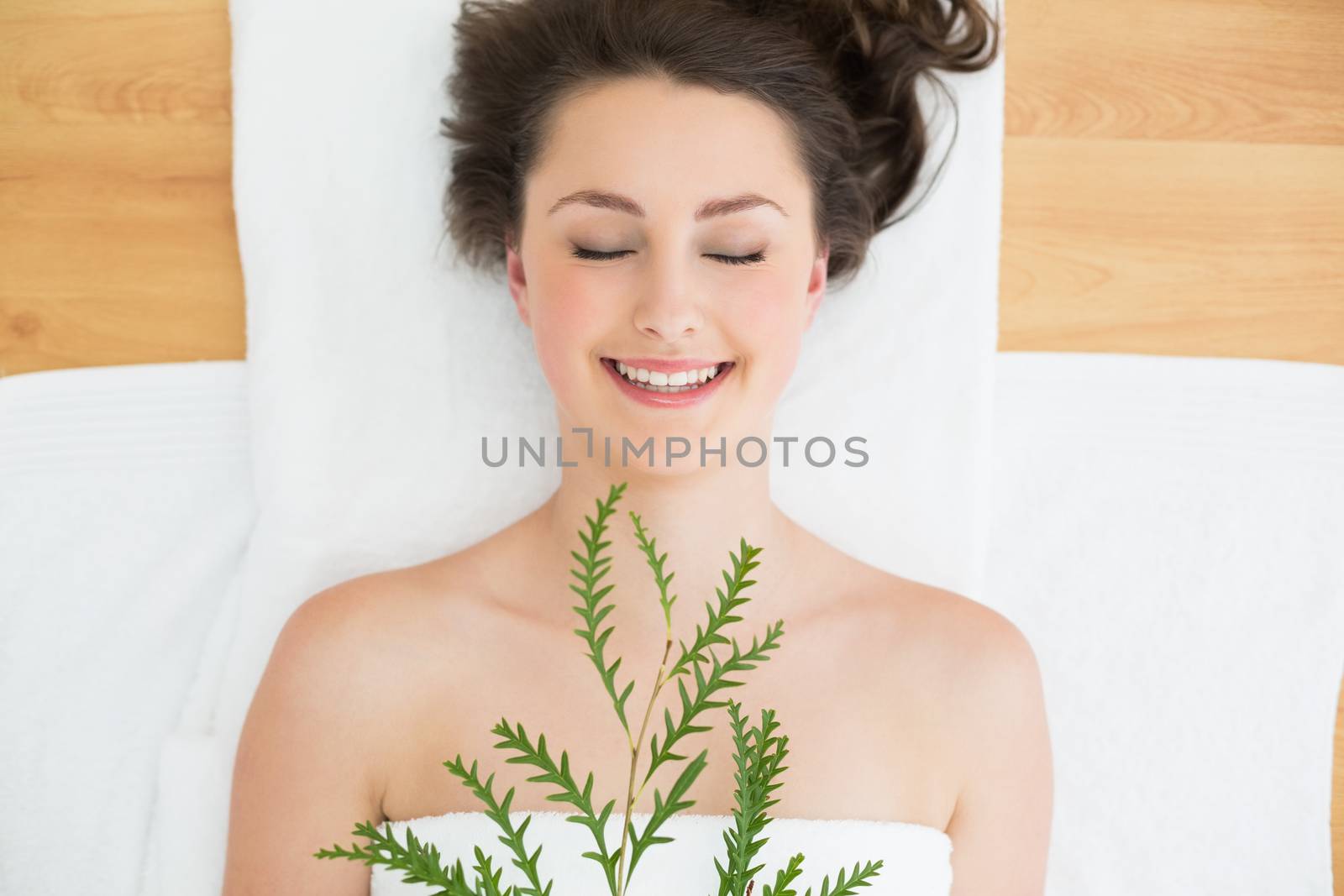 Overhead view of a young brunette lying with leaves on massage table in beauty salon