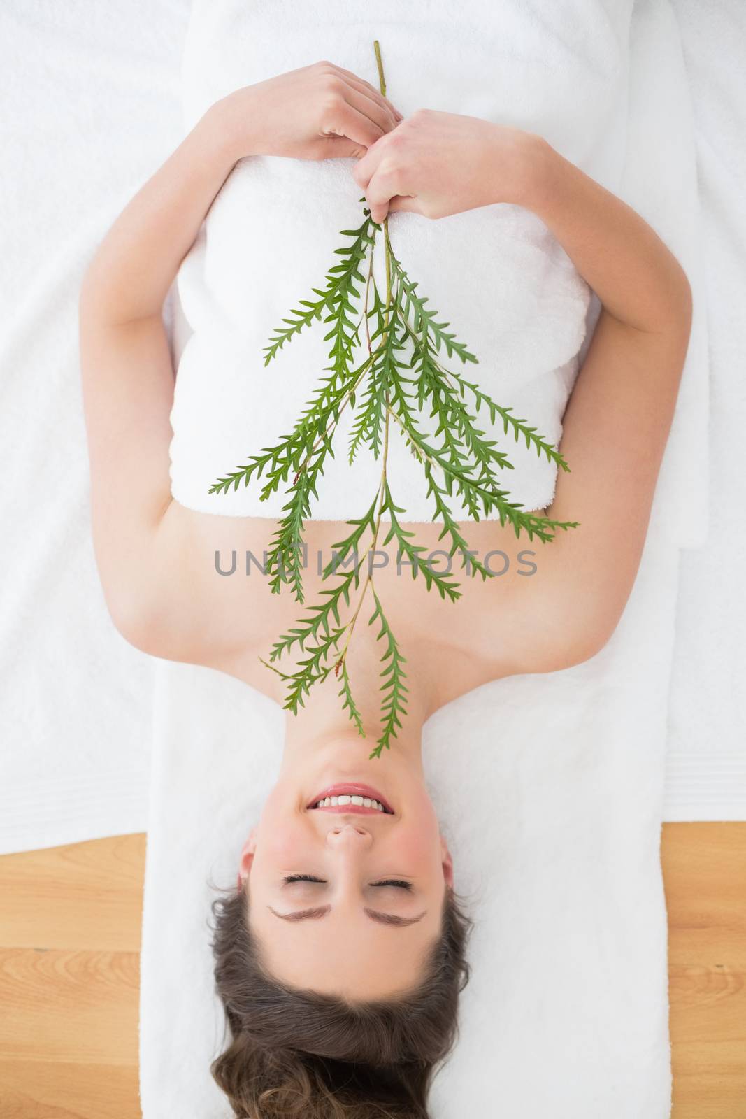 Overhead view of a young brunette lying with leaves on massage table in beauty salon