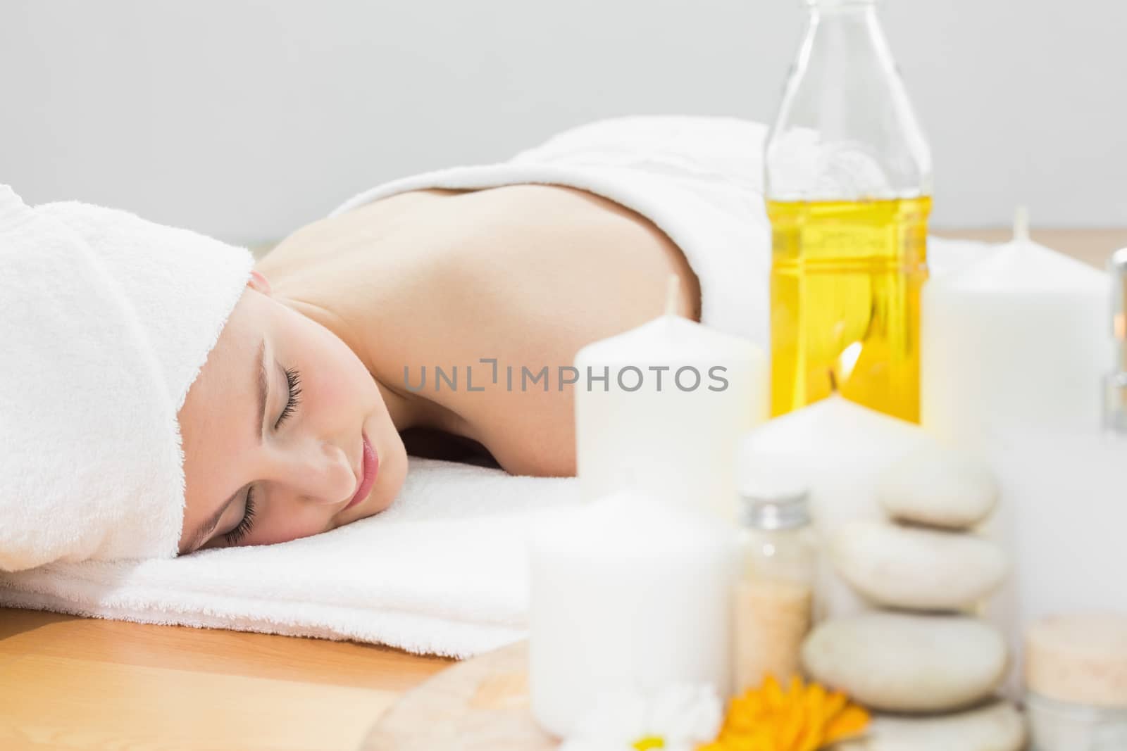 Beautiful young woman resting with oil bottle in foreground at beauty spa