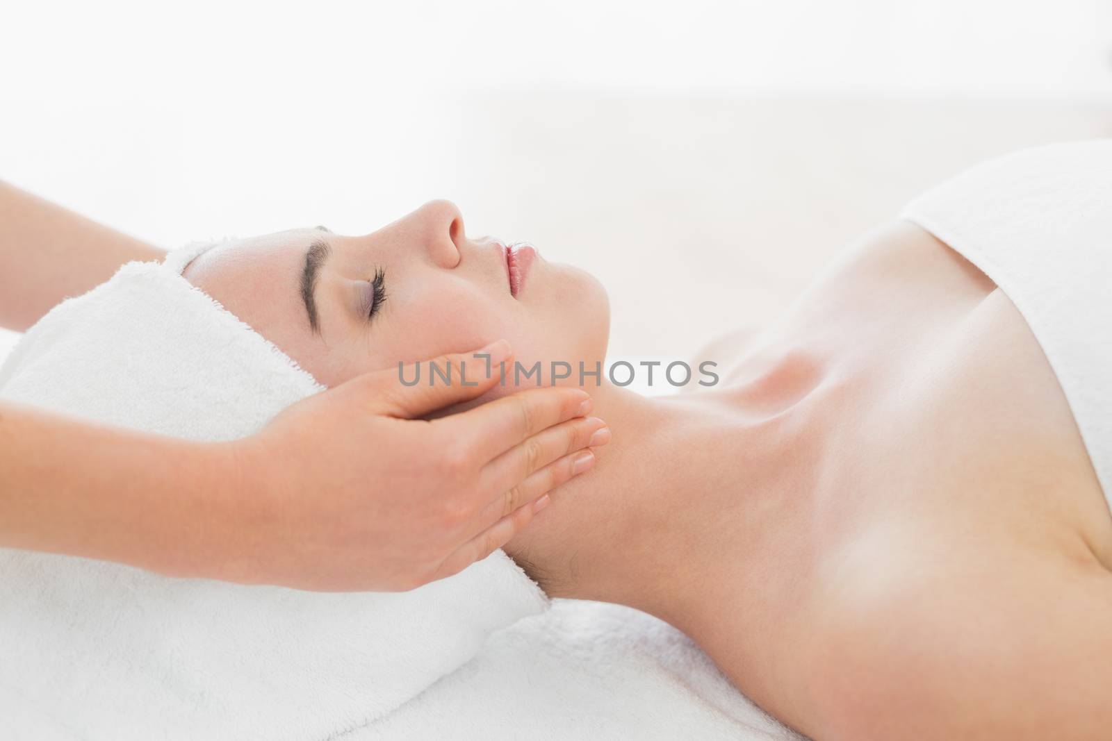Side view of hands massaging a beautiful womans face at beauty spa
