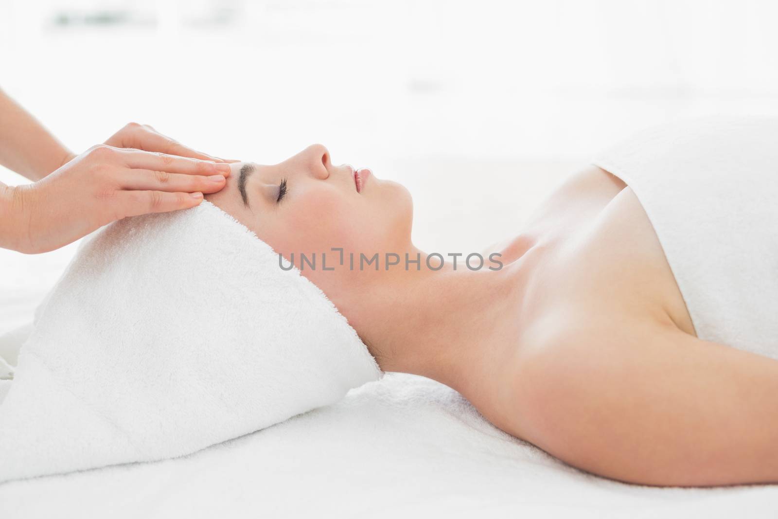 Side view of hands massaging a beautiful womans forehead at beauty spa