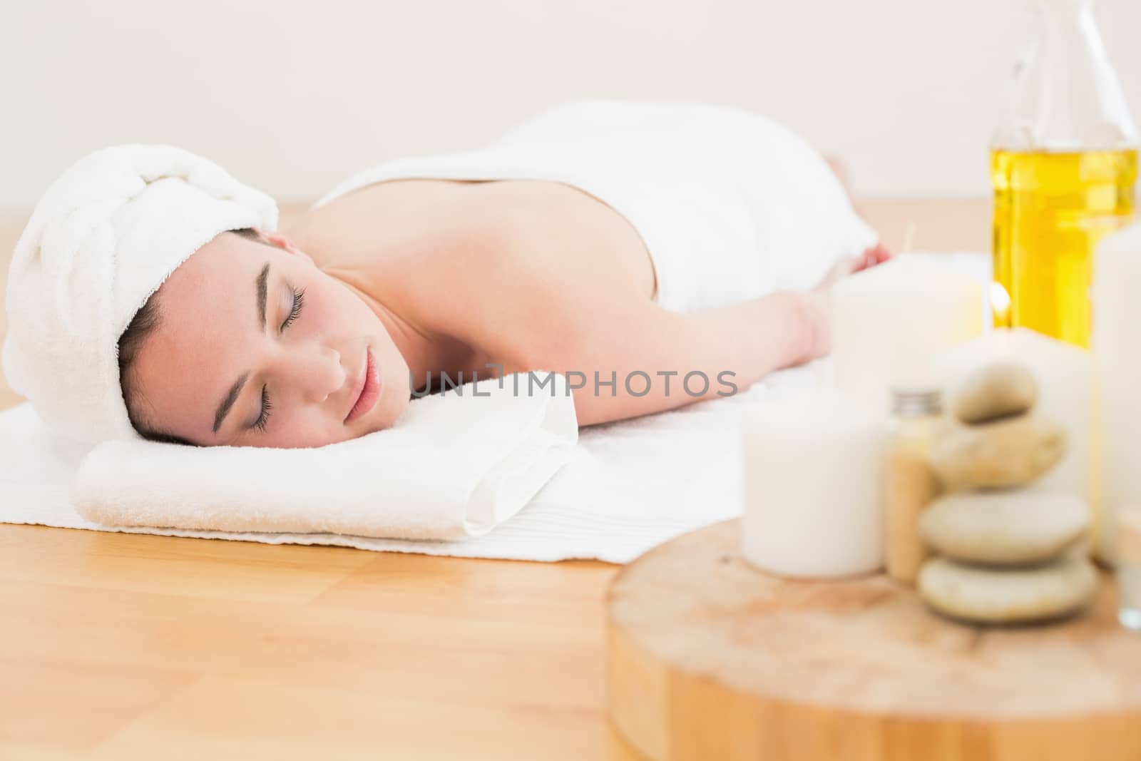 Beautiful young woman resting with oil bottle in foreground at beauty spa