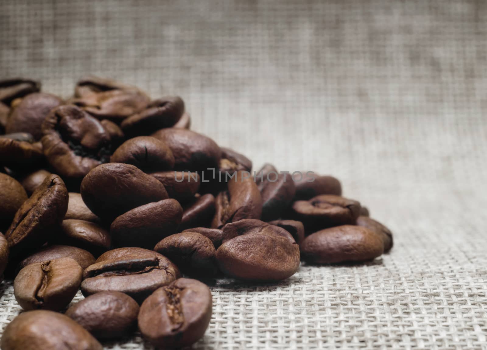 heap of roasted coffee beans on a matting macro beige background closeup