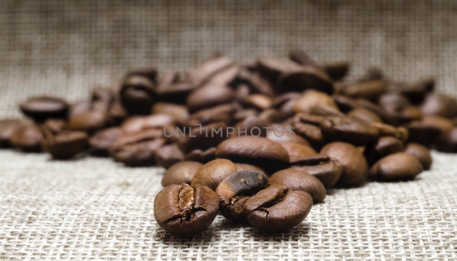 heap of roasted coffee beans on a matting macro beige background closeup