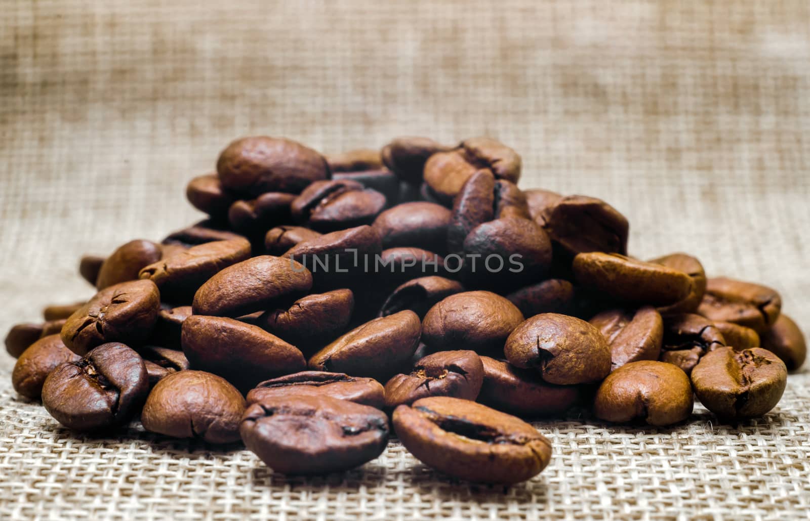 heap of coffee beans on a matting macro beige background closeup
