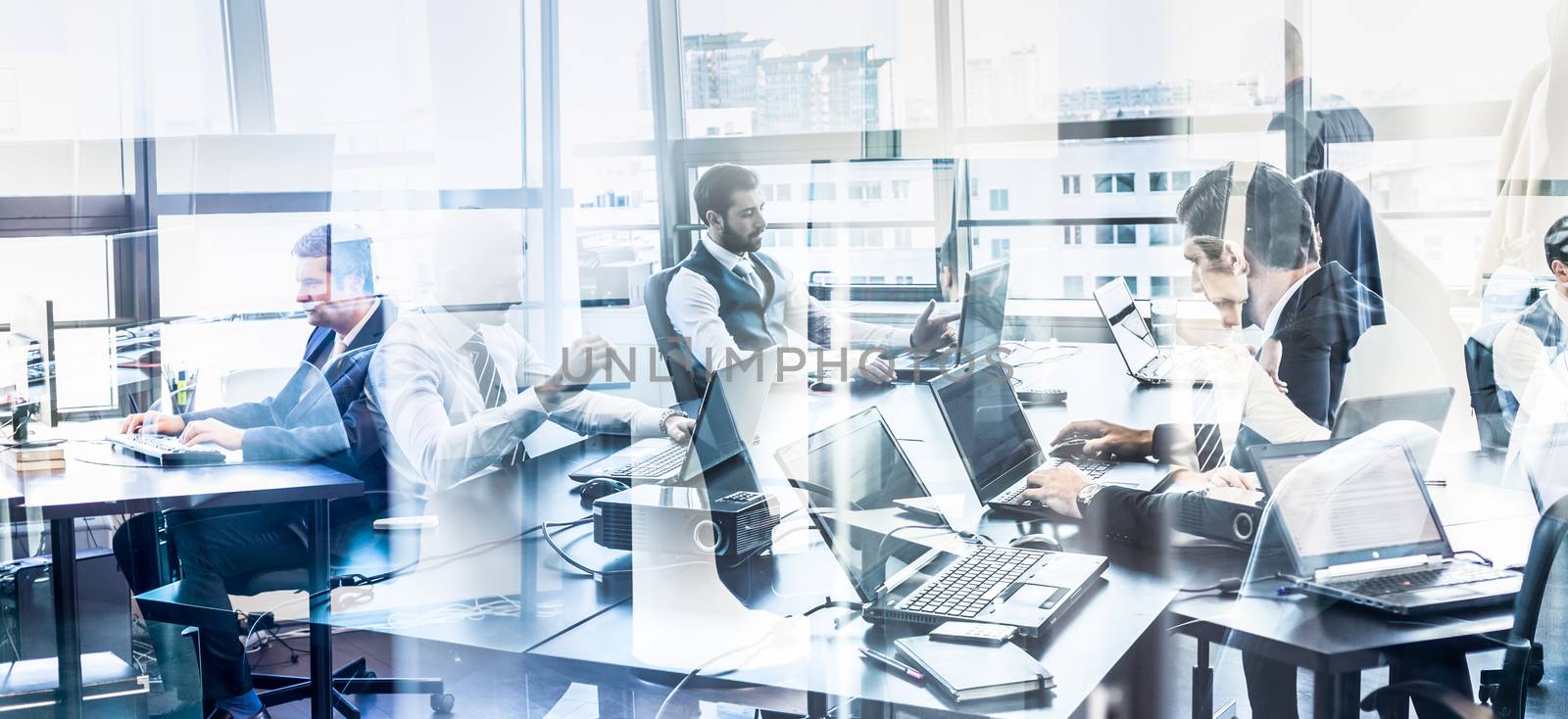 Workplace in modern corporate office with business people working on their laptops. Window reflections. Business and Entrepreneurship concept.