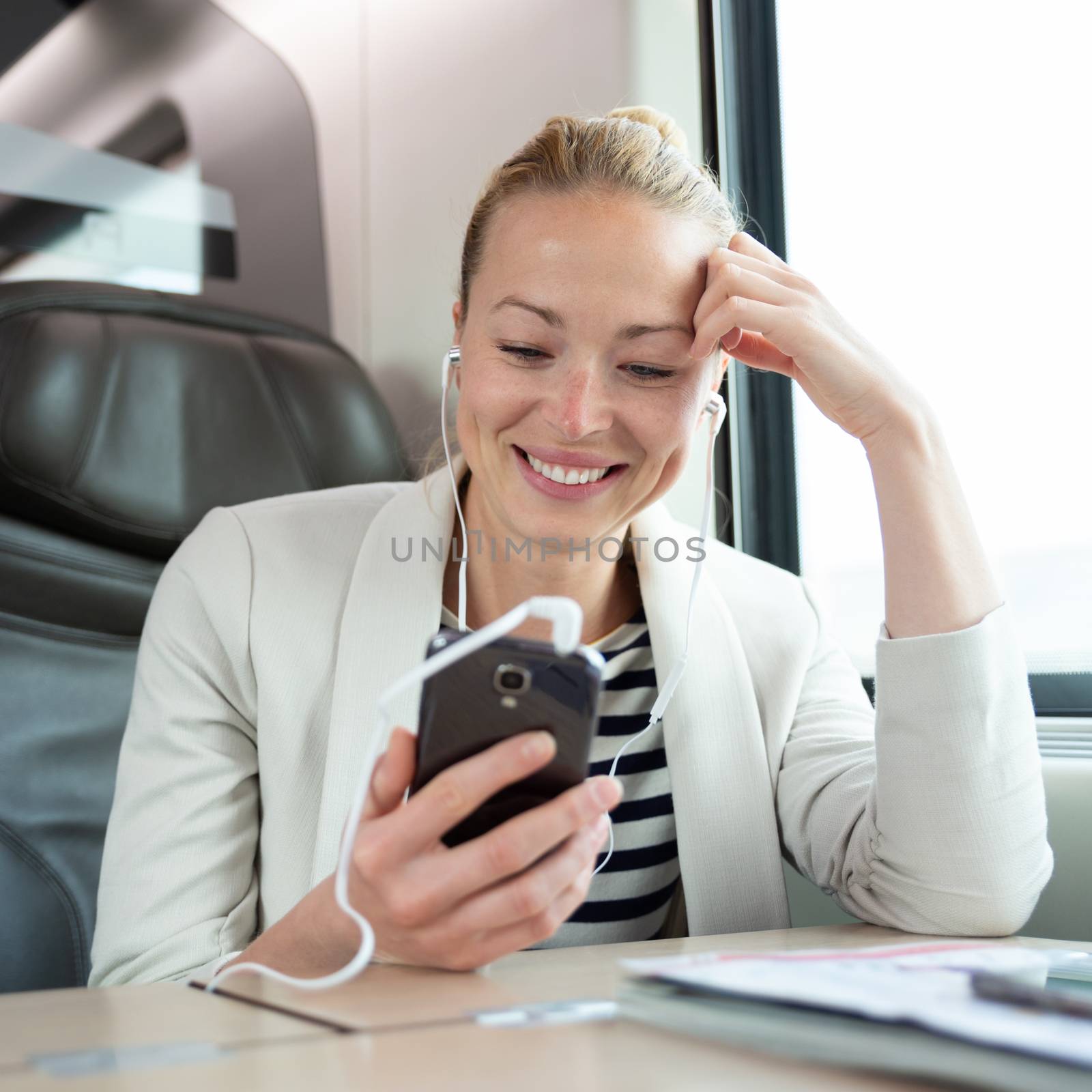 Businesswoman communicating on cellphone using headphone set while traveling by train in business class seat.