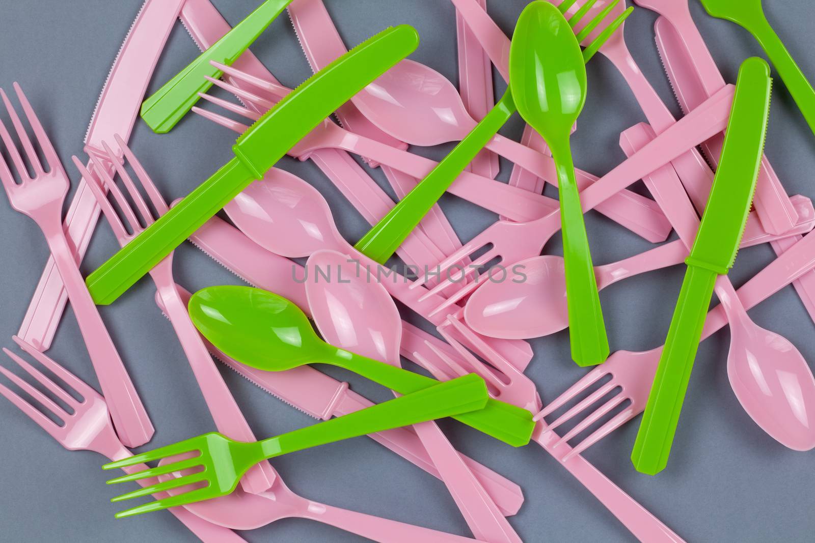 Background from reusable recyclable pink and green forks, spoons, knifes made from corn starch on grey paper. Eco, zero waste, alternative to plastic concept. Flat lay, top view. Horizontal. Closeup.