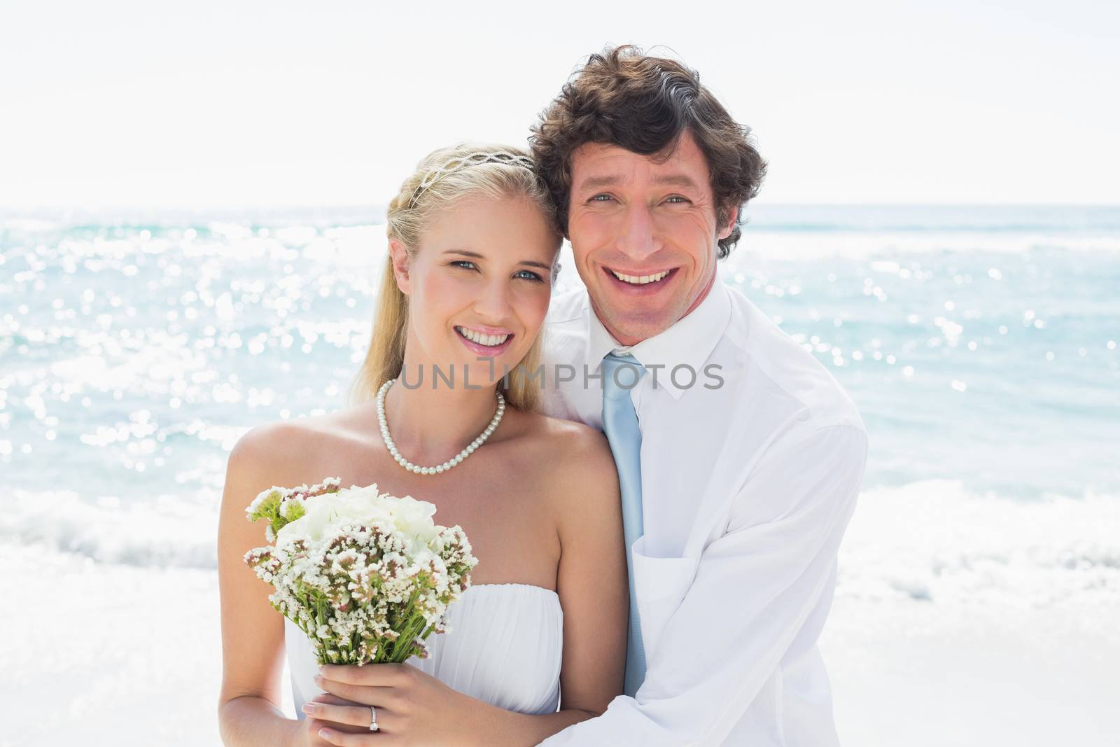 Romantic couple on their wedding day smiling at camera at the beach