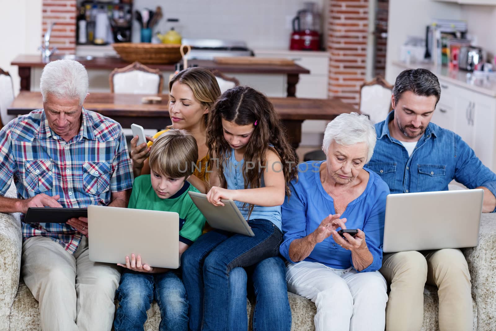Multi-generation family using a laptop, tablet and phone by Wavebreakmedia