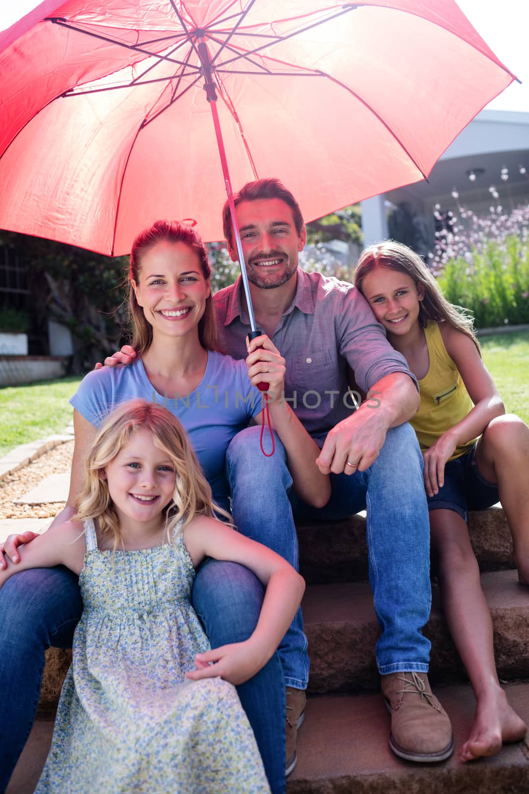 Happy family sitting in garden under a red umbrella on a sunny day