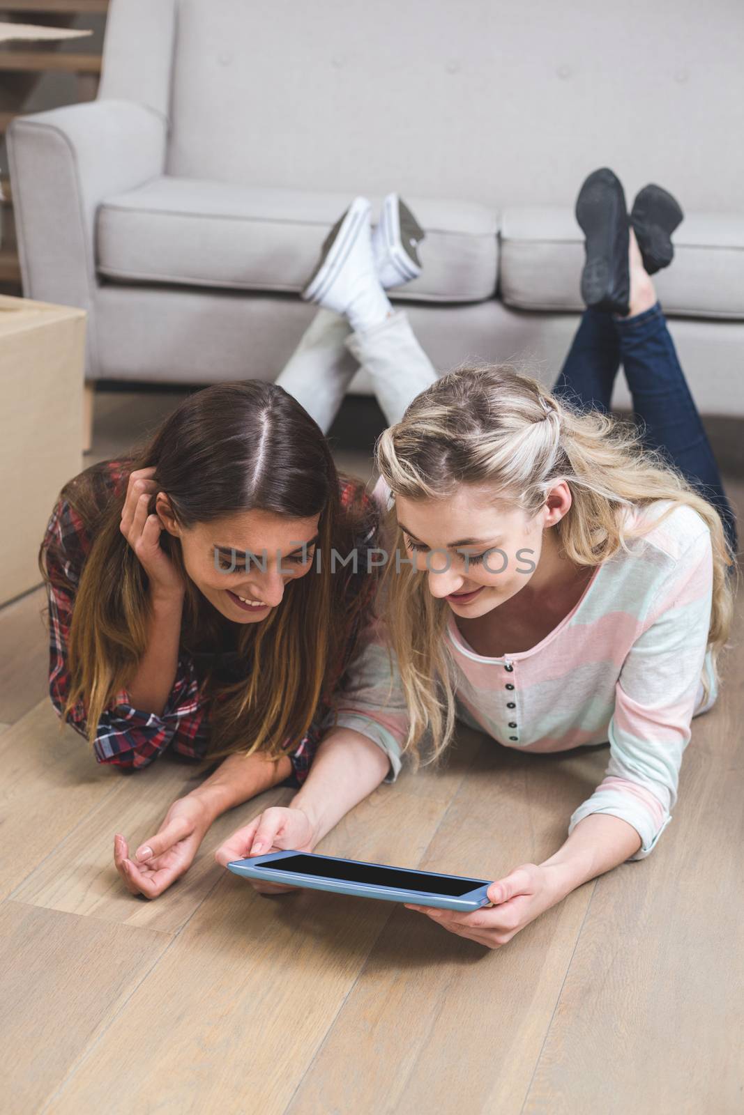 Friends lying together on the floor and using digital tablet in their new house