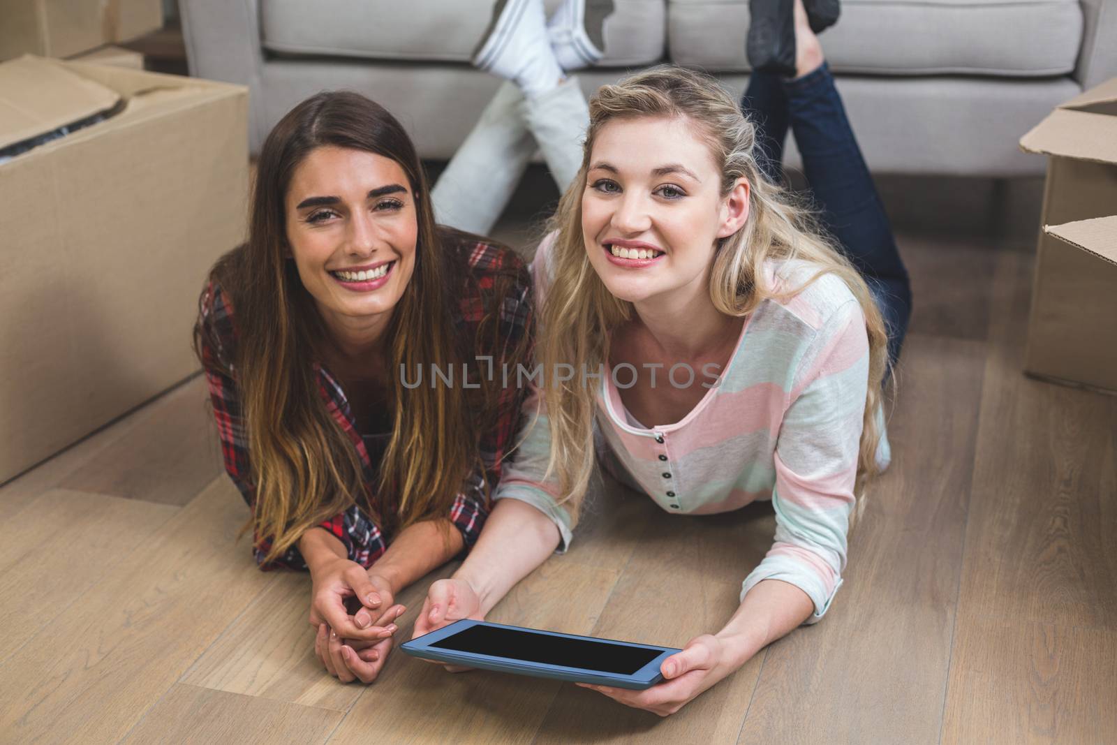 Friends lying together on the floor and using digital tablet in their new house