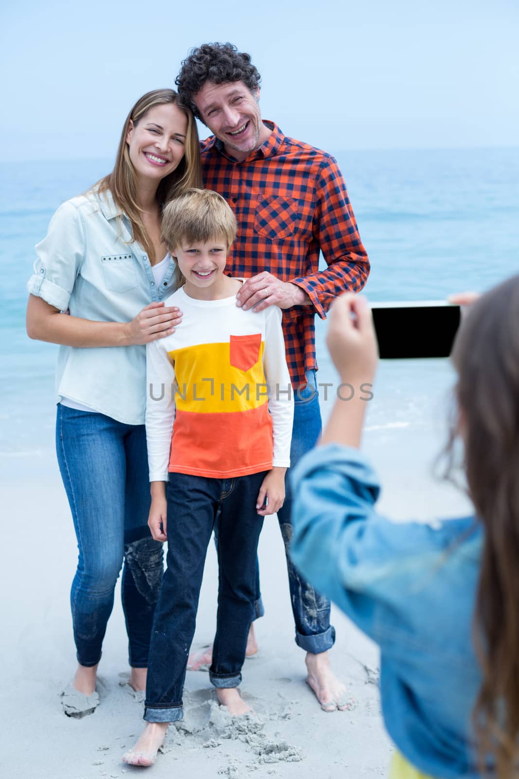 Girl photographing happy family with mobile phone at sea shore