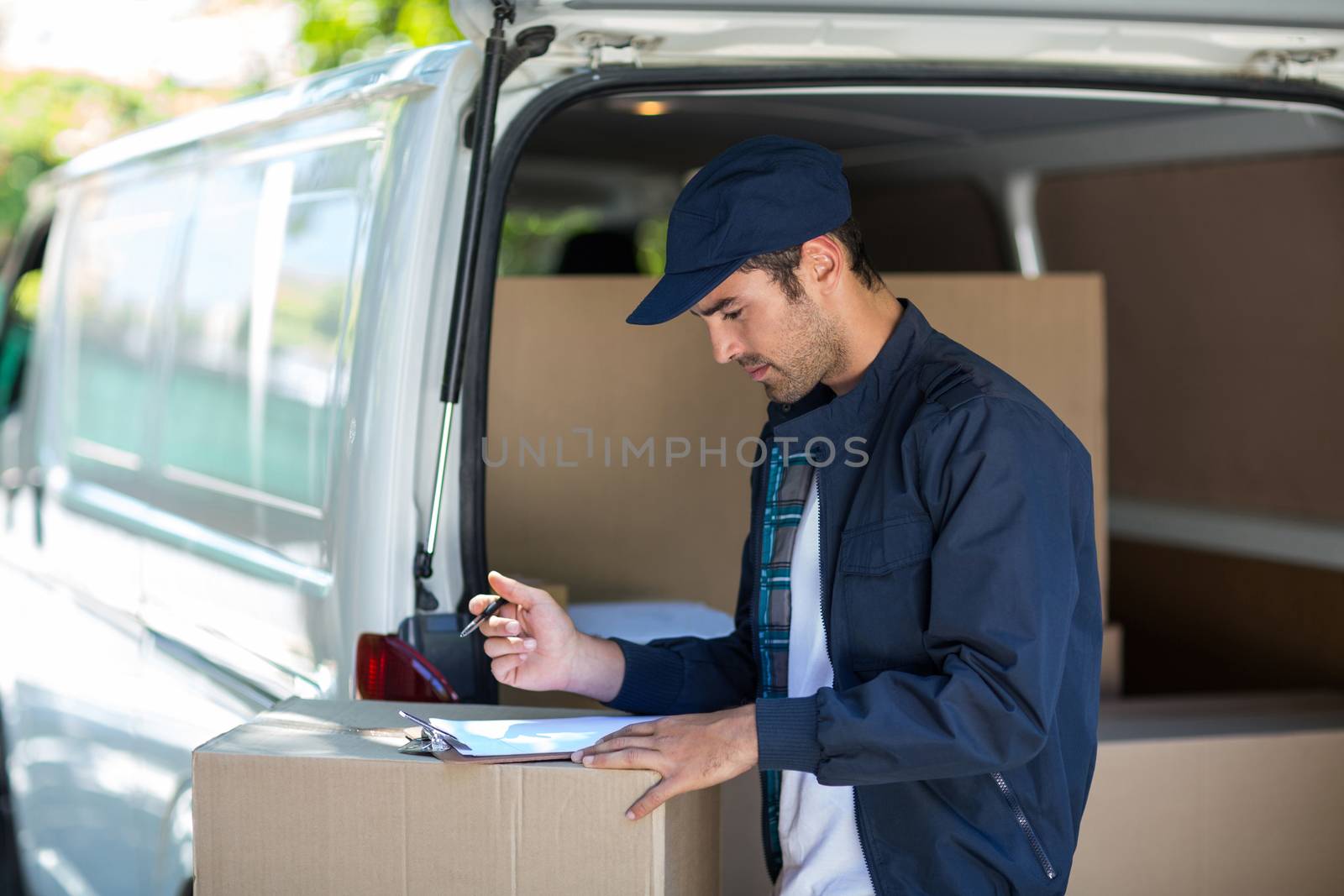 Side view of delivery person writing in clipboard while standing by van