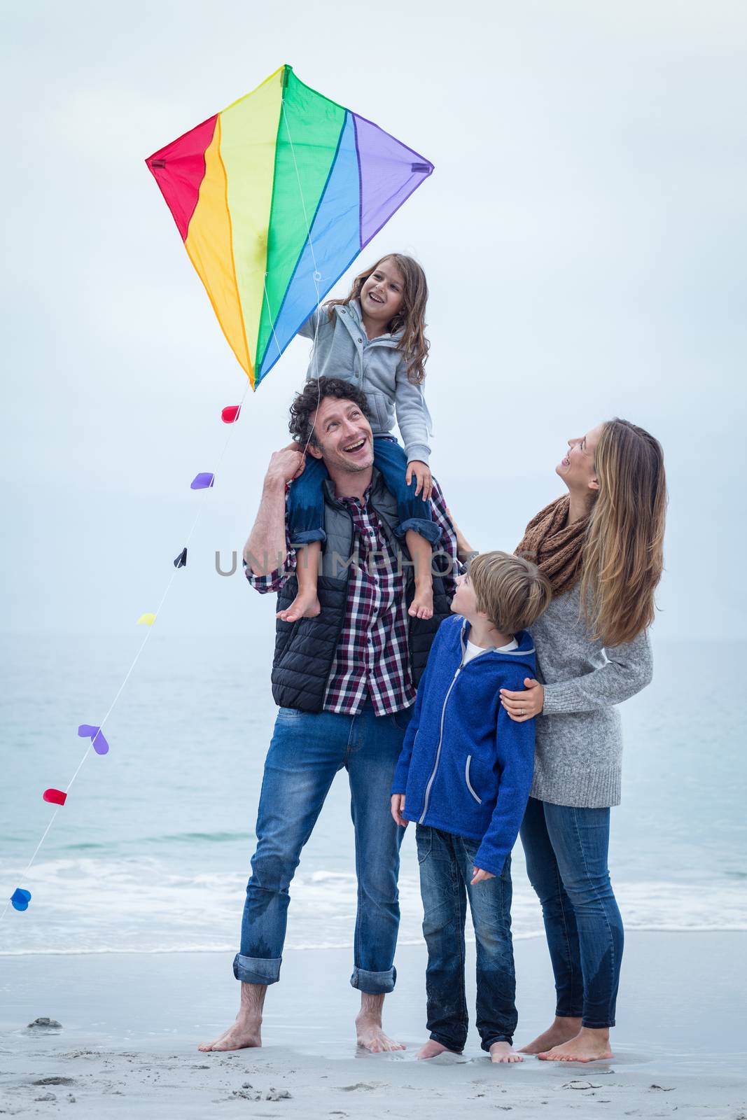 Full length of cheerful family with kite standing at sea shore