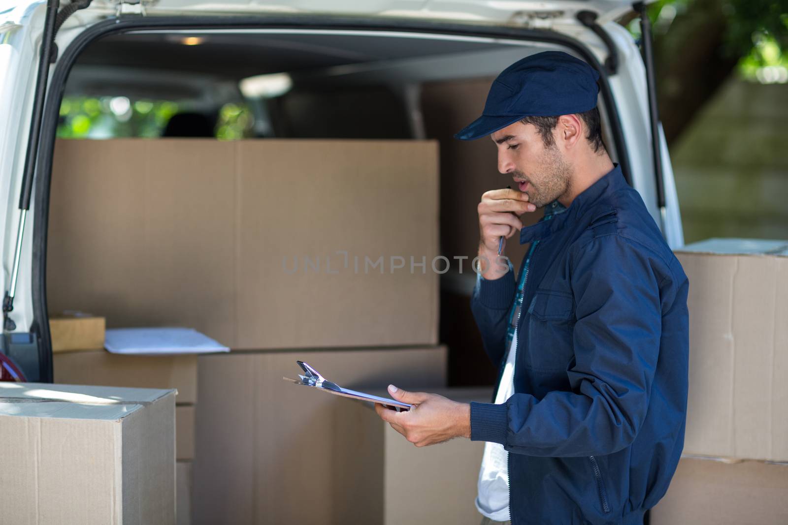 Thoughtful delivery man holding clipboard while standing by van