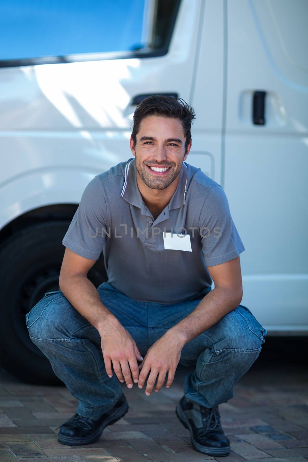 Portrait of smiling delivery man crouching by van