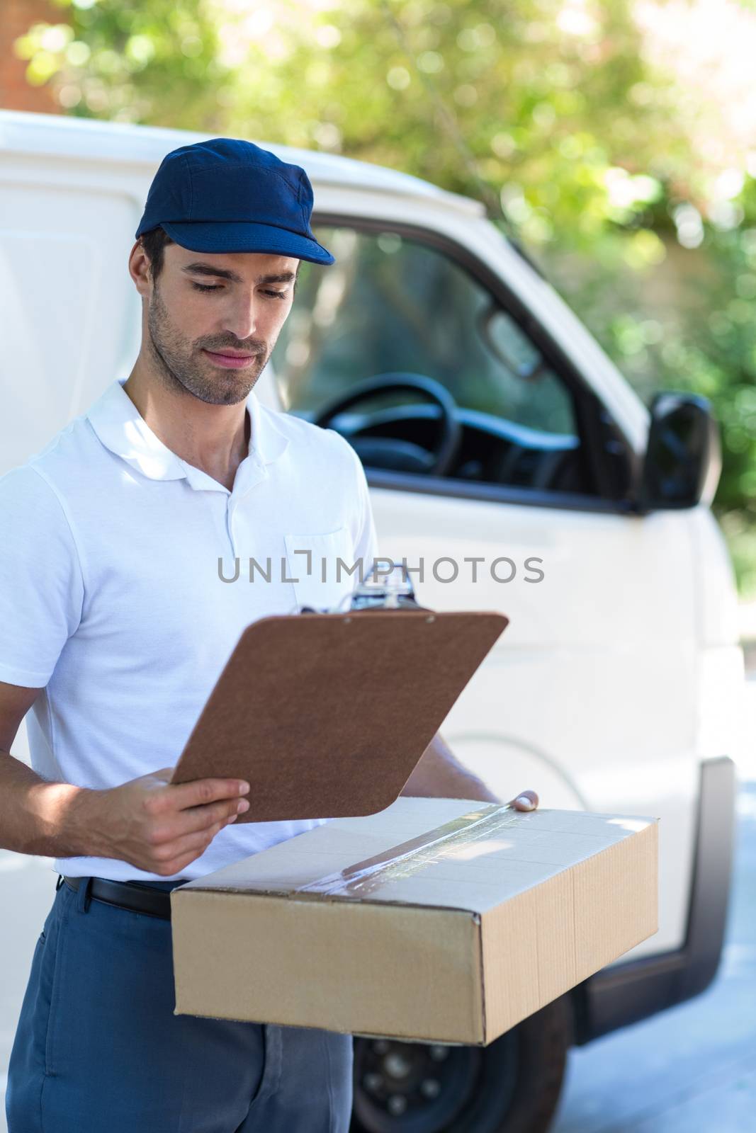 Delivery man looking at clipboard while standing by van
