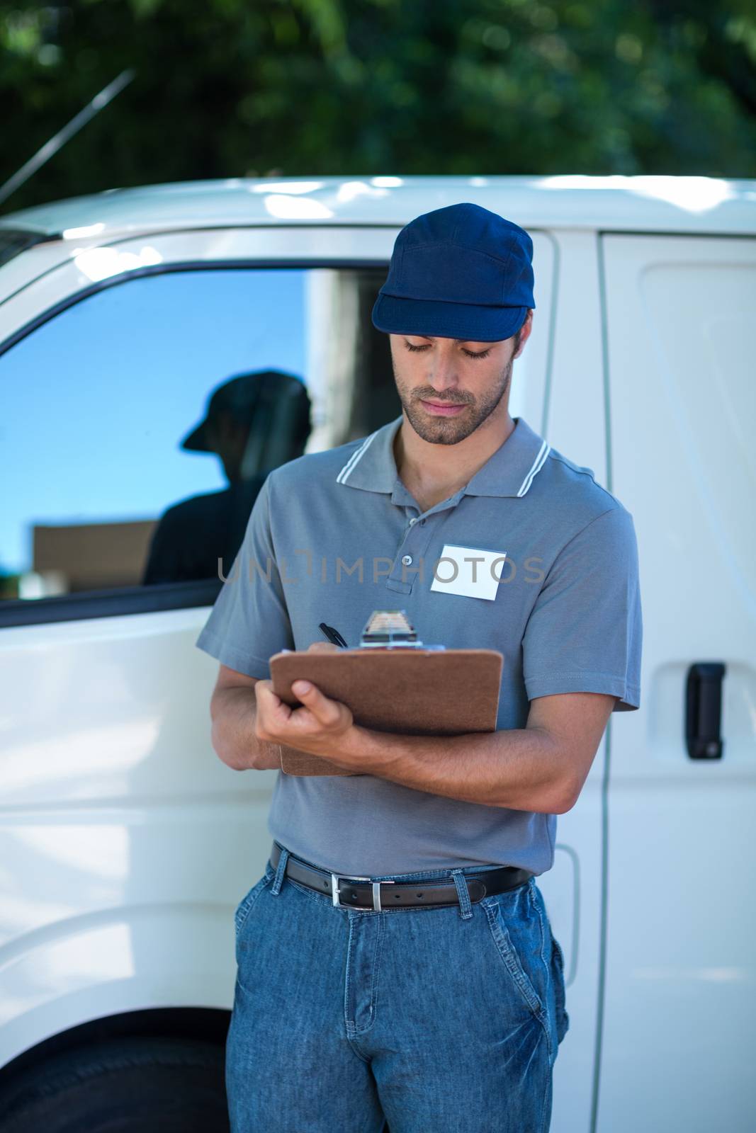 Delivery person writing in clipboard while standing by van