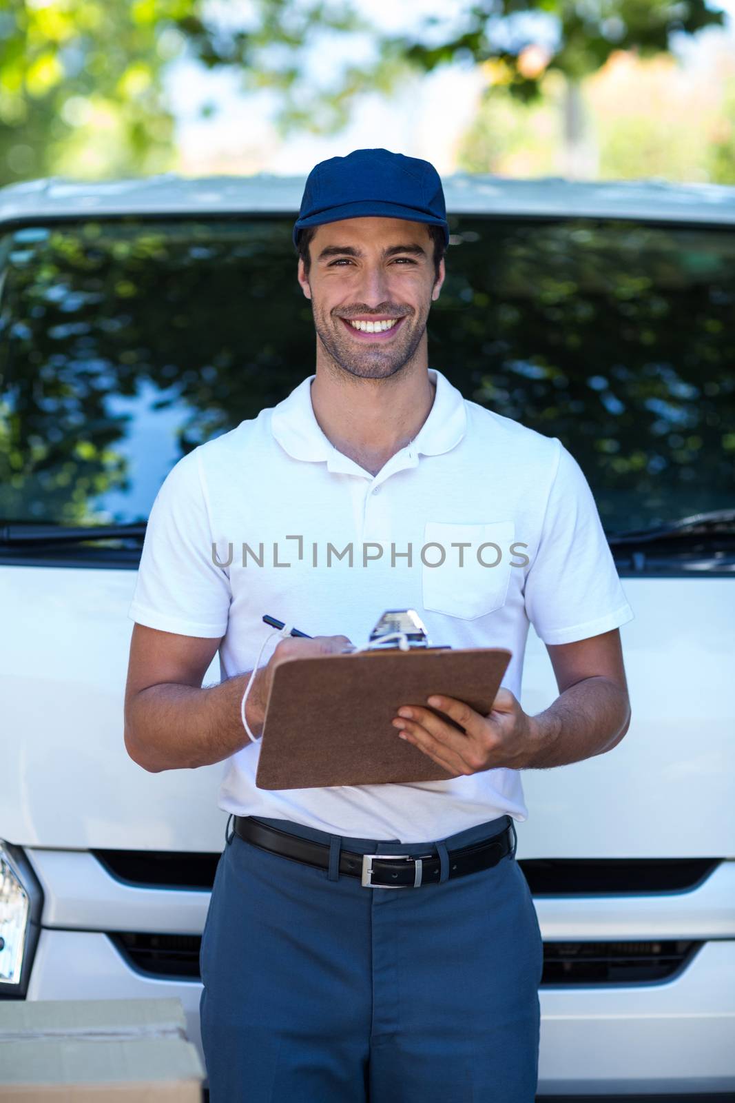 Portrait of smiling delivery man writing in clipboard while standing by van