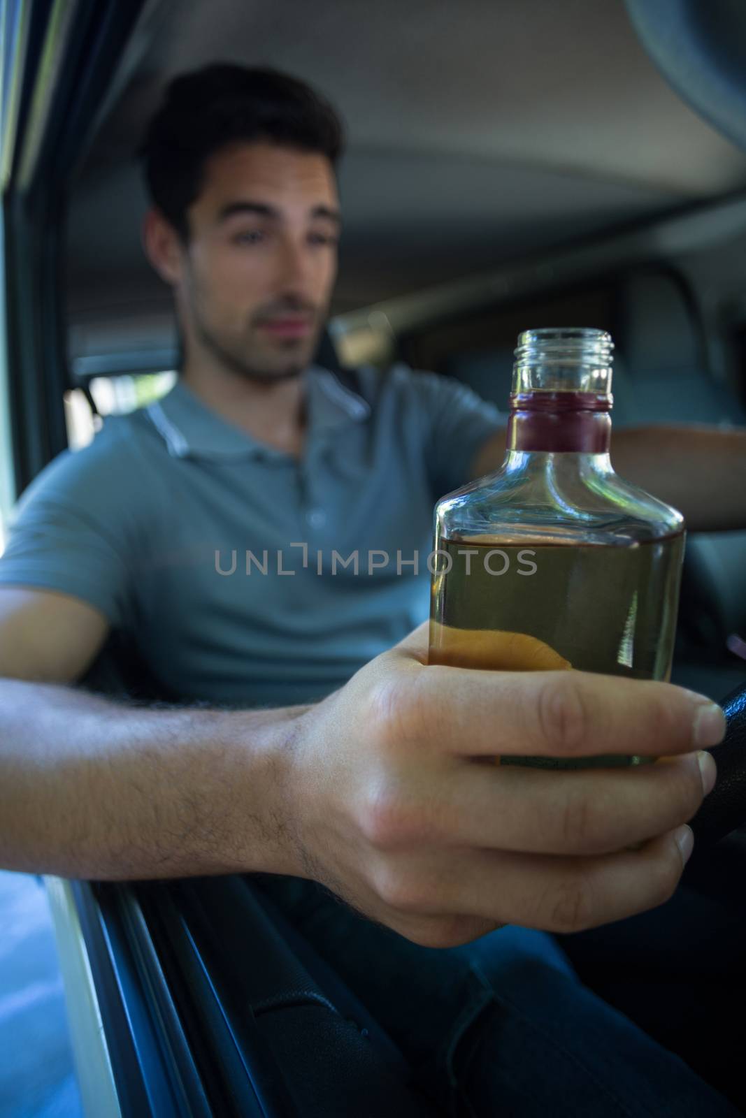 Slumped young man holding alcohol bottle while driving car